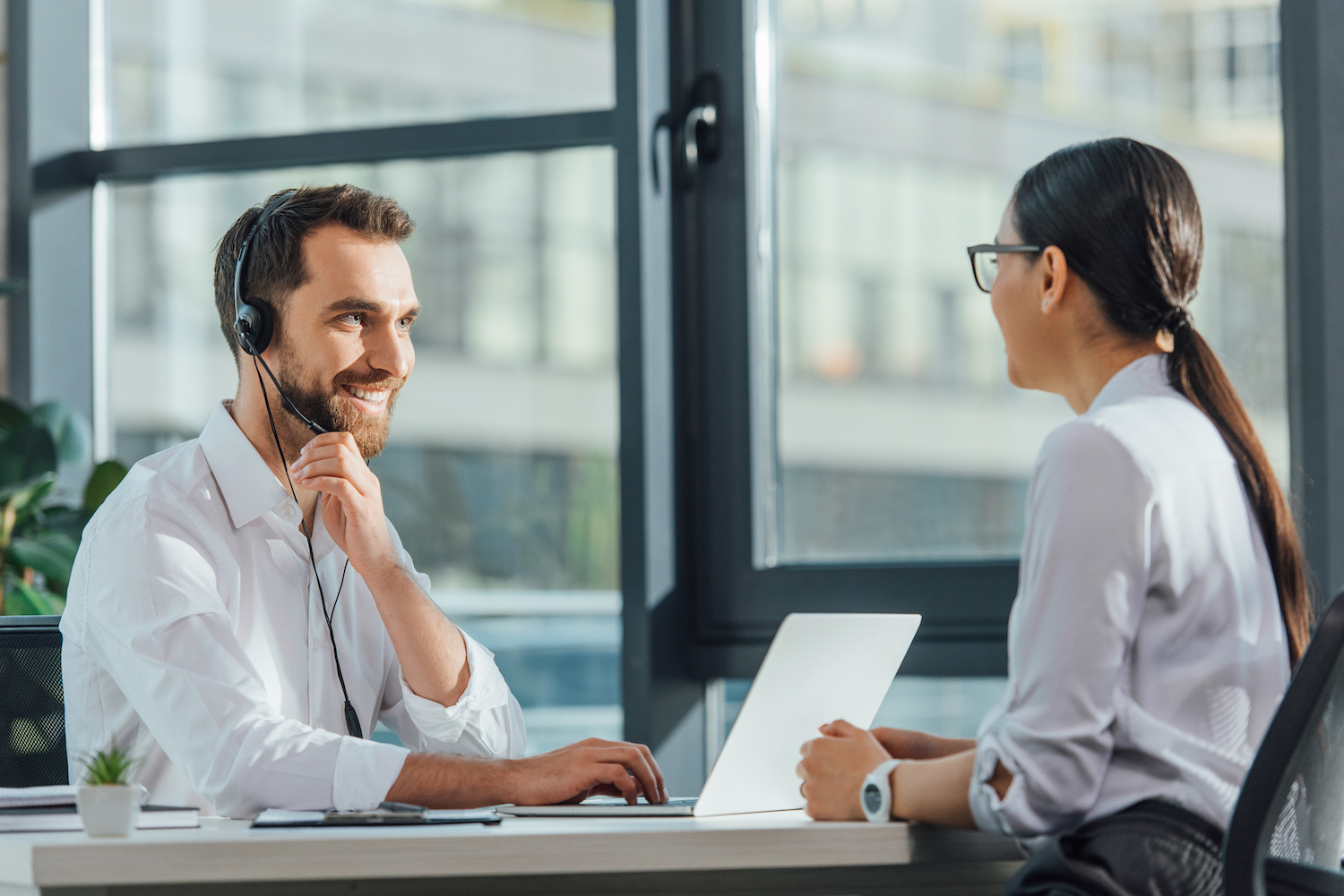 smiling male translator working online with laptop and headset on meeting with businesswoman